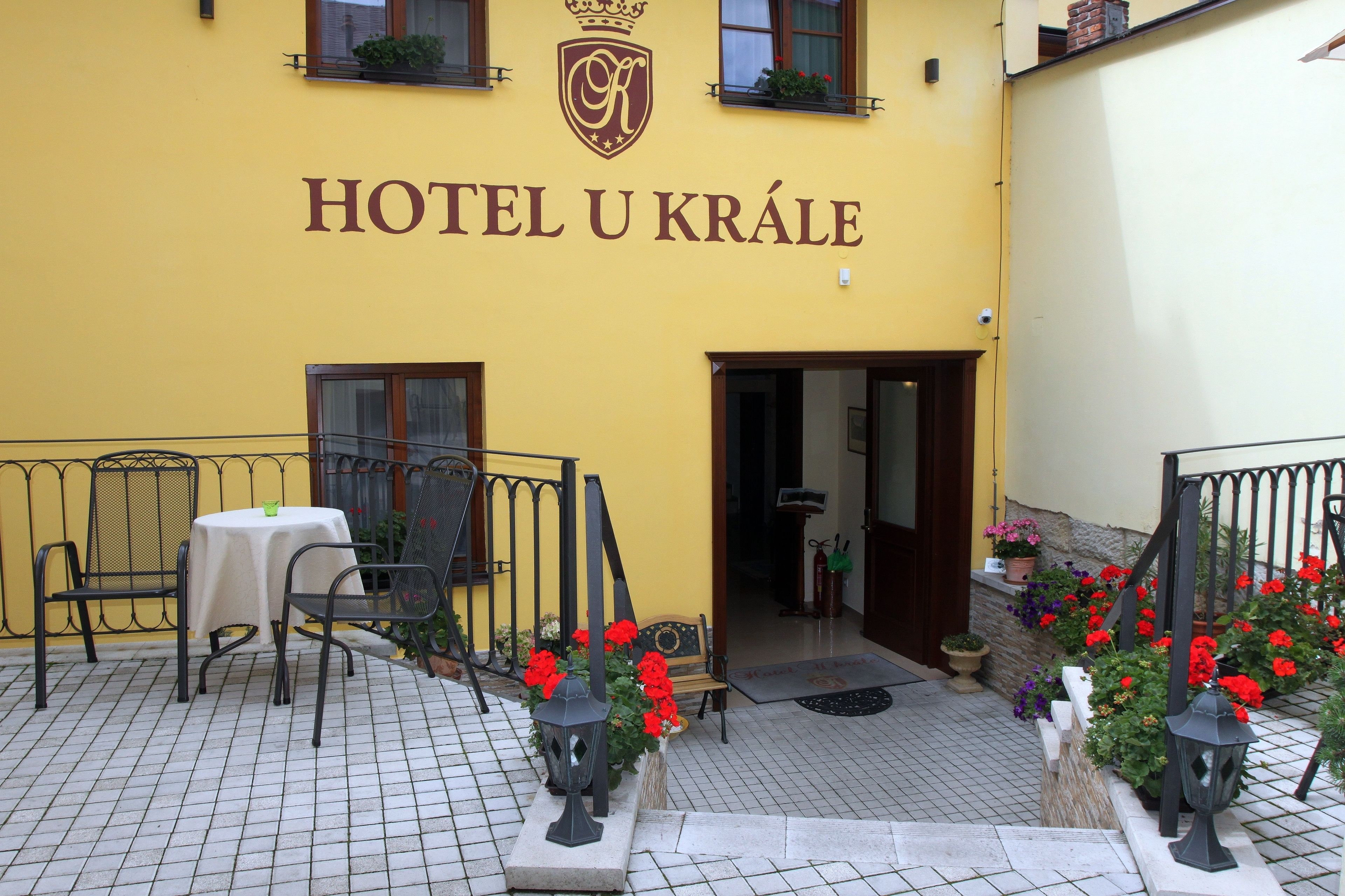 A yellow building with the sign "HOTEL U KRÁLE" and outdoor seating with tables and chairs.