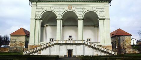 A large, white building with a central arched entrance and a staircase leading up to it.