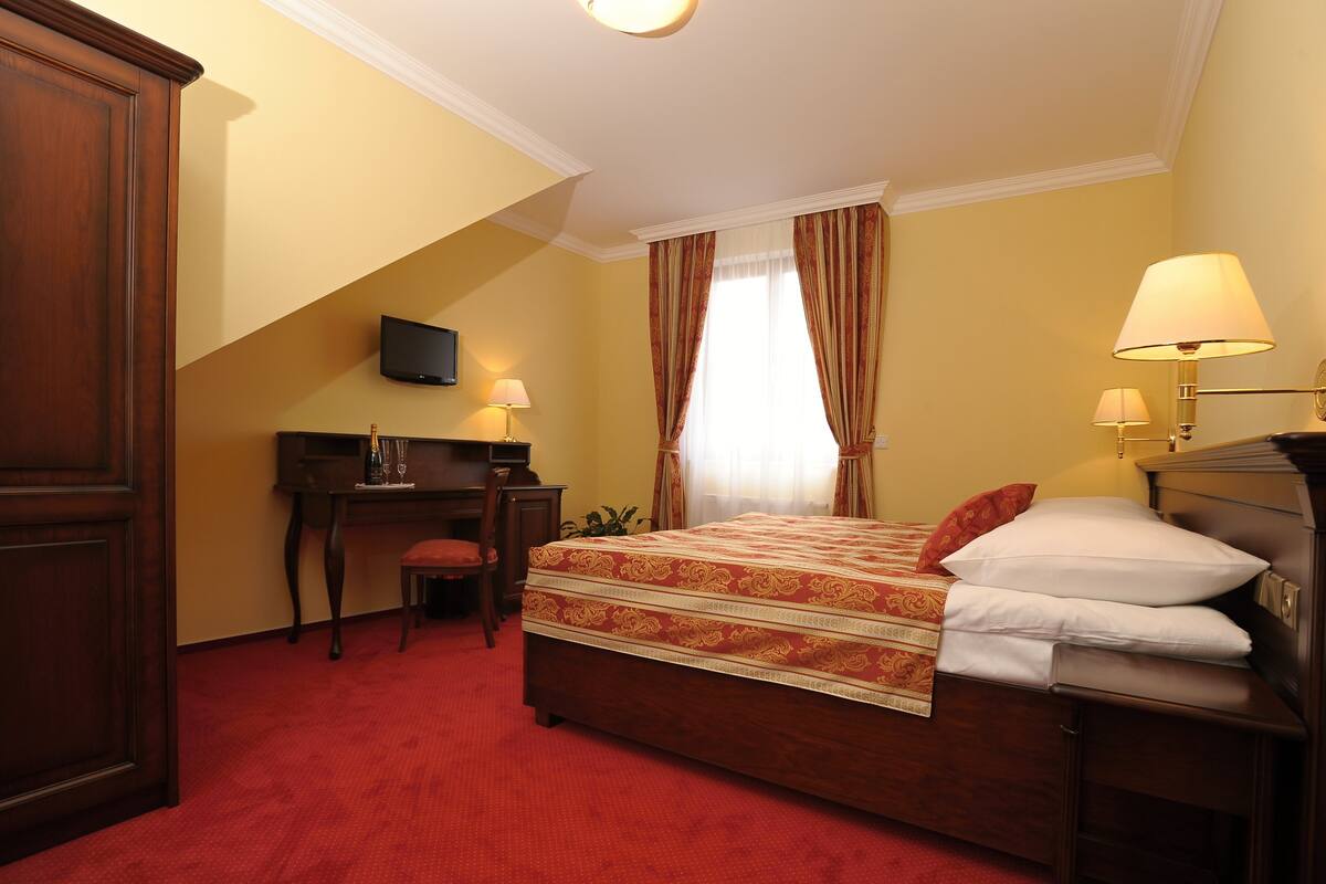 A hotel room with a bed, desk, chair, and a TV mounted on the wall.