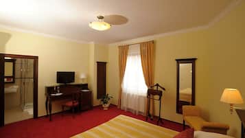 A hotel room with a bed, a desk with a computer, a chair, a TV, a mirror, and a window with curtains.