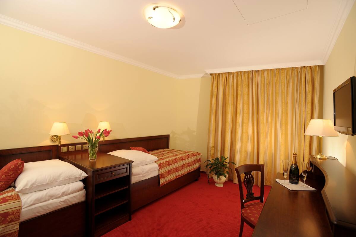 A hotel room with two single beds, a wooden desk with a lamp, a television, and a red carpet.