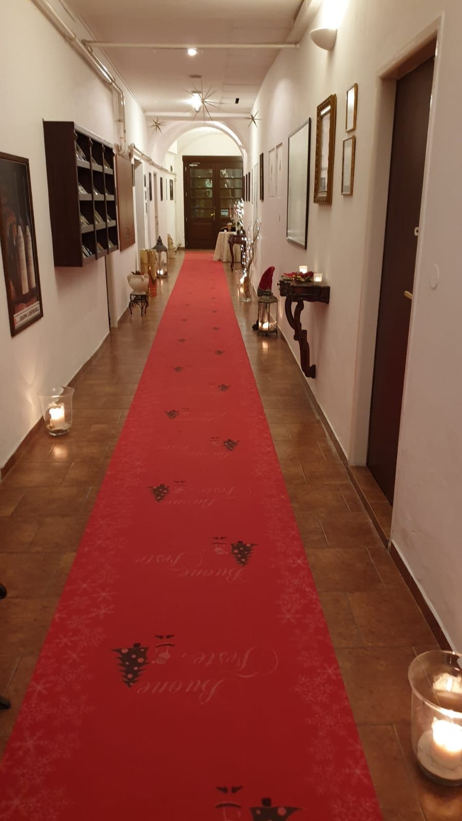 Un pasillo con alfombra roja, cuadros en las paredes y una puerta al final.