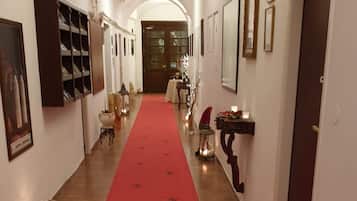 Un pasillo con alfombra roja, cuadros en las paredes y una puerta al final.