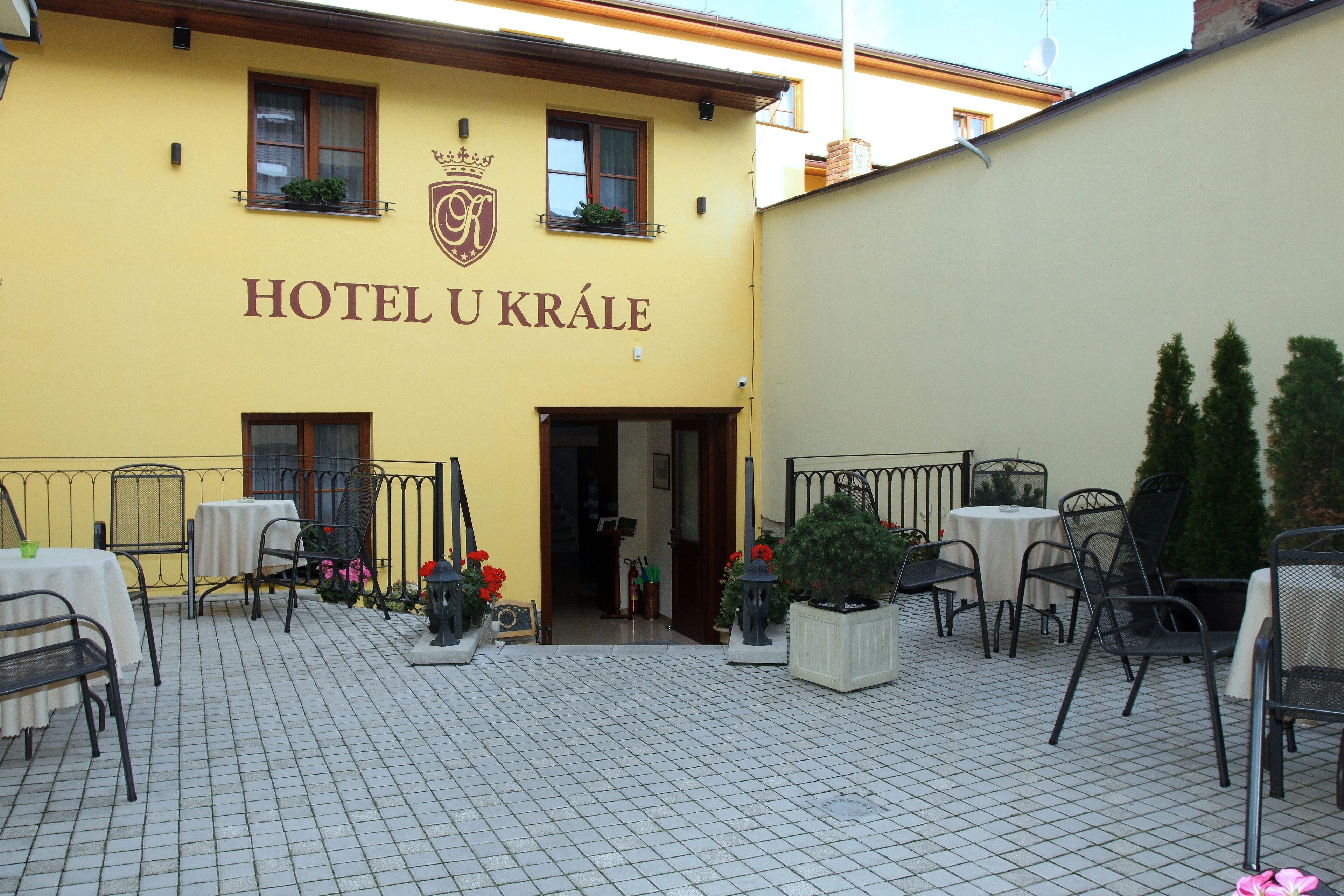 A yellow building with the sign "HOTEL U KRÁLE" and outdoor seating with tables and chairs.