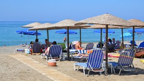 A beach with sun loungers and umbrellas, a wooden walkway, and a calm sea. - Galeana Beach Hotel (Rethymno)