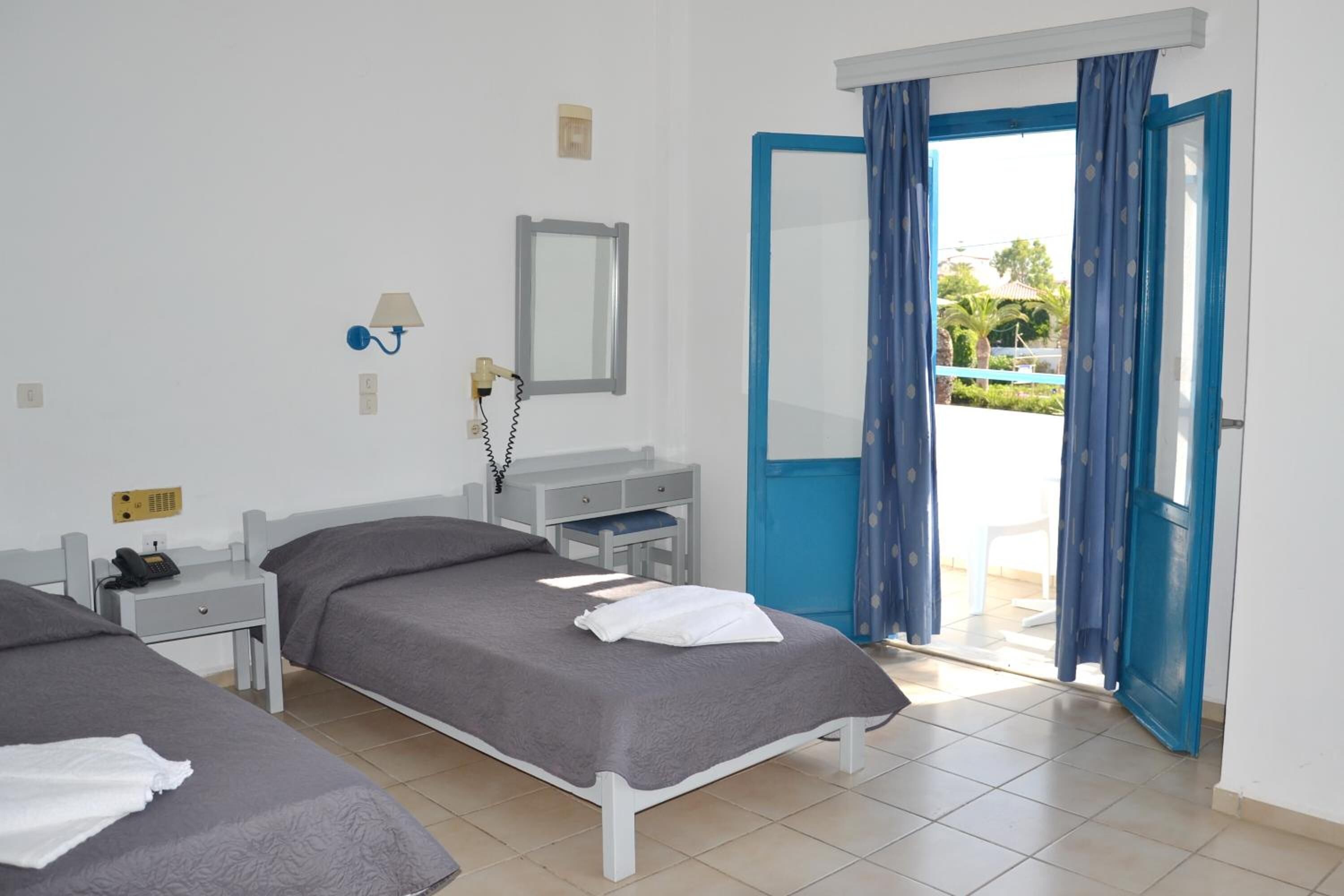 A hotel room with two beds, a desk, a telephone, a mirror, and a door leading to a balcony.