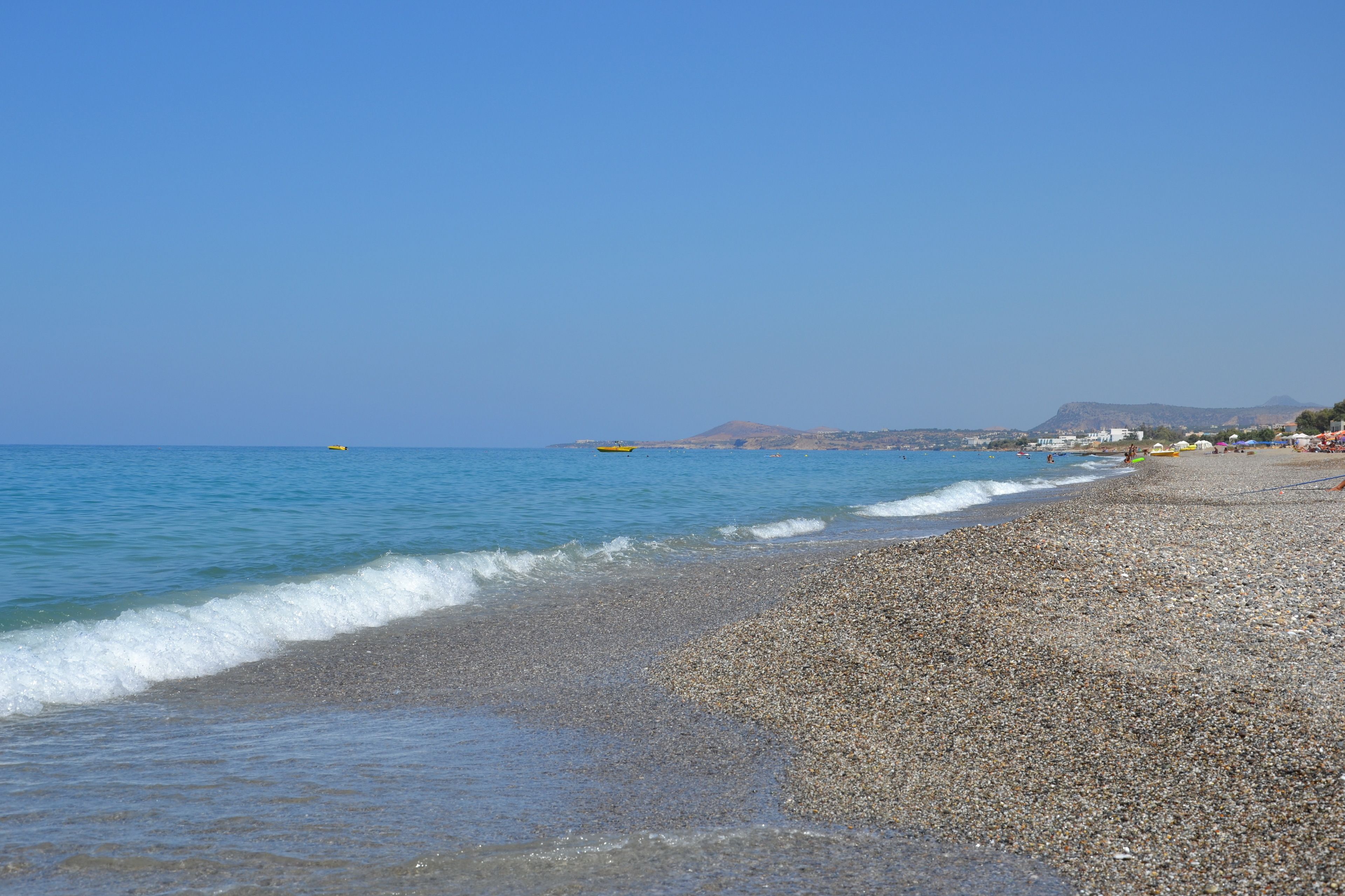 Ein Kiesstrand mit klarem, blauem Wasser und einem entfernten Berg.