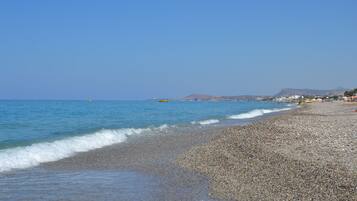 Ein Kiesstrand mit klarem, blauem Wasser und einem entfernten Berg.