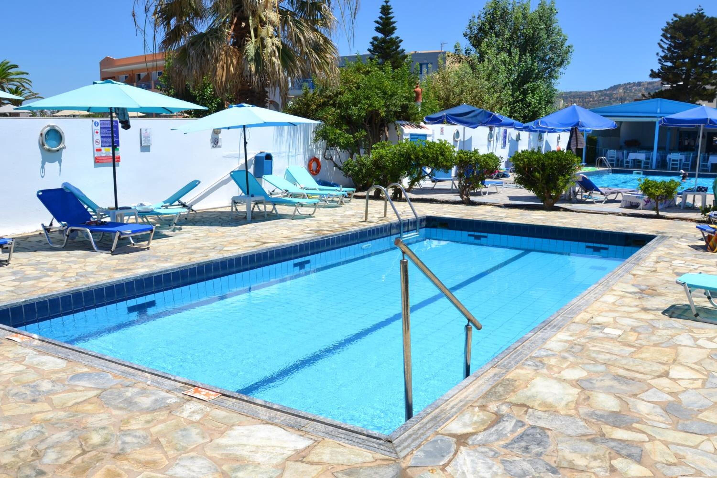 Una piscina amb aigua blava, envoltada de gandules i ombrel·les.