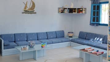 Ett vardagsrum med en blå soffa, två soffbord i glas, en bokhylla och en dekorativ väggdekoration i form av en segelbåt.