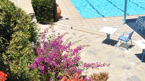 A swimming pool with lounge chairs and umbrellas, surrounded by greenery and a clear view of the sea. - Galeana Beach Hotel (Rethymno)