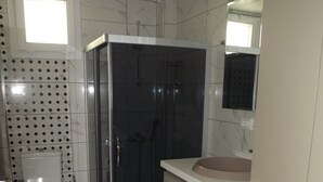 Un baño pequeño con inodoro, ducha con mampara de vidrio, lavadora y lavamanos.