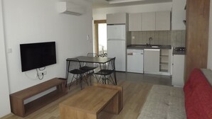 A compact living space with a kitchenette, a dining area with a table and chairs, a TV mounted on the wall, and a bench. - Opus Apart Hotel (Kusadasi)