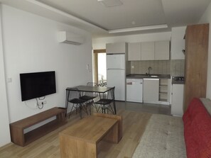A compact living space with a kitchenette, a dining area with a table and chairs, a TV mounted on the wall, and a bench. - Opus Apart Hotel (Kusadasi)