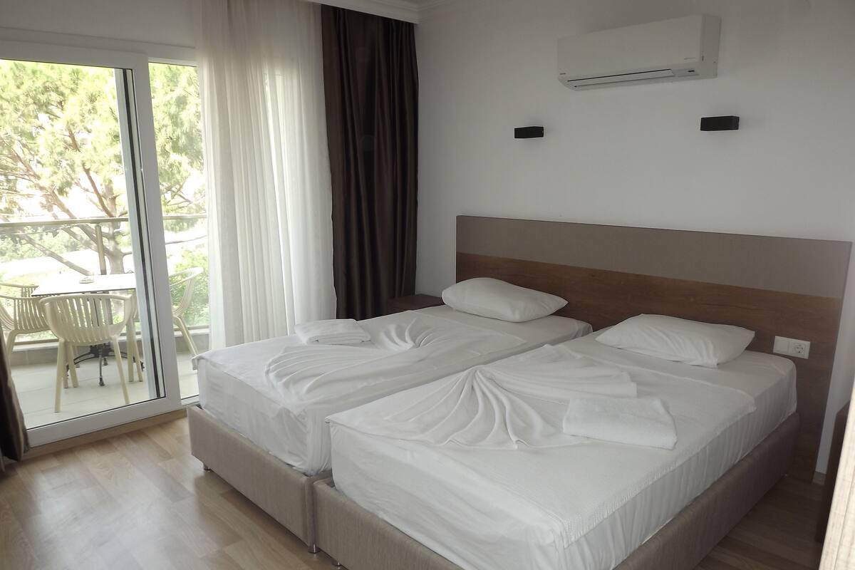 A hotel room with two beds, a sliding glass door to a balcony, and an air conditioning unit on the wall.
