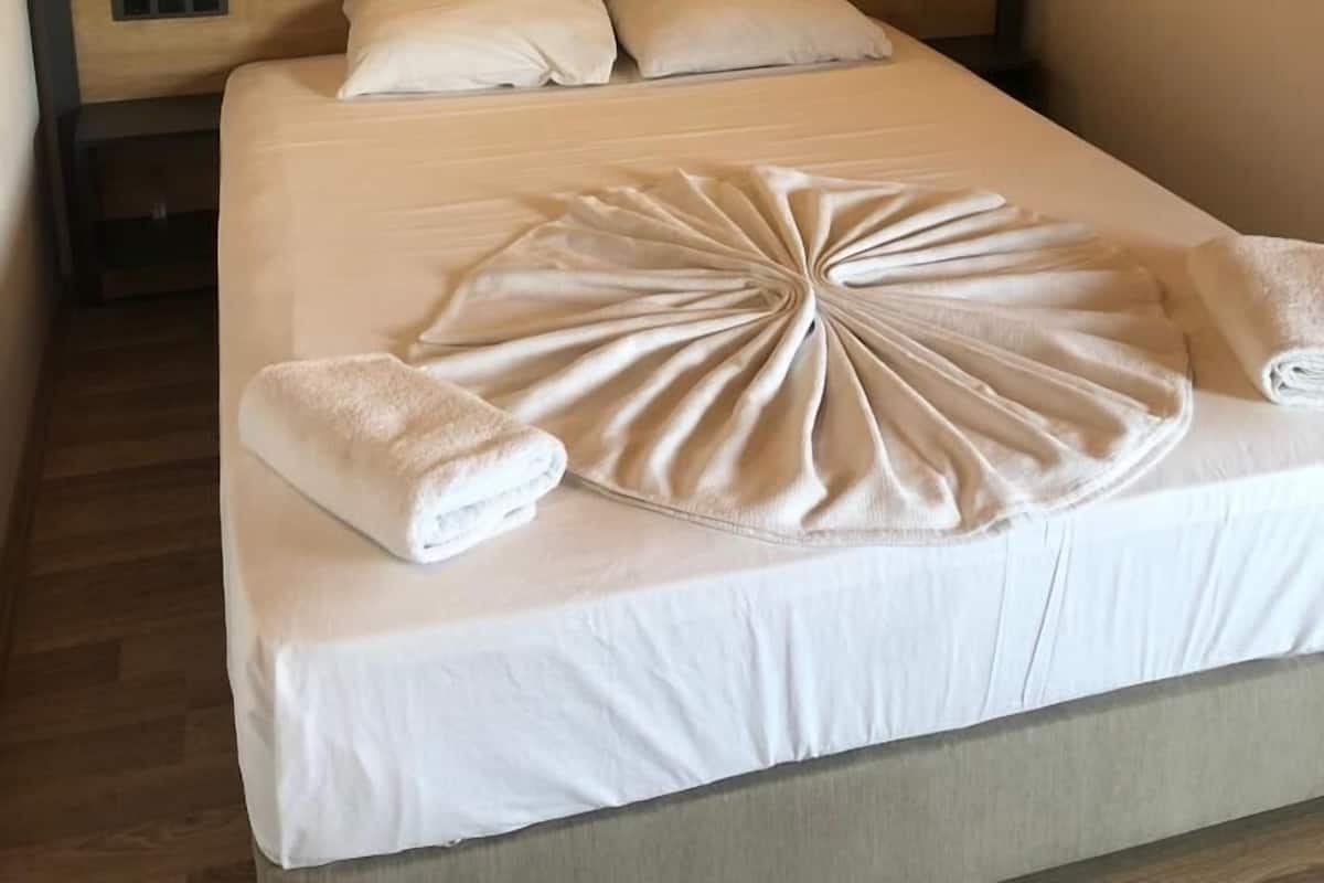 A neatly made bed with a white comforter and pillows, a wooden headboard, and two wall-mounted lights.