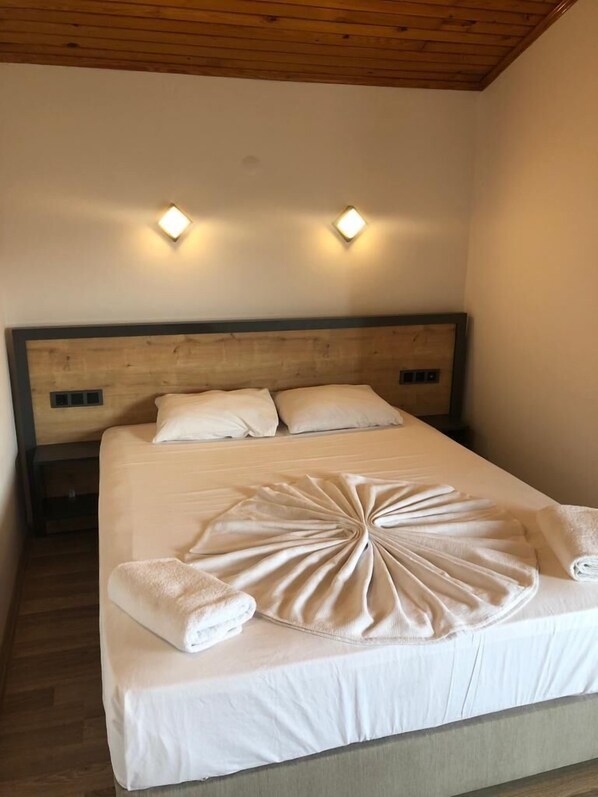 A neatly made bed with a white comforter and pillows, a wooden headboard, and two wall-mounted lights. - Opus Apart Hotel (Kusadasi)