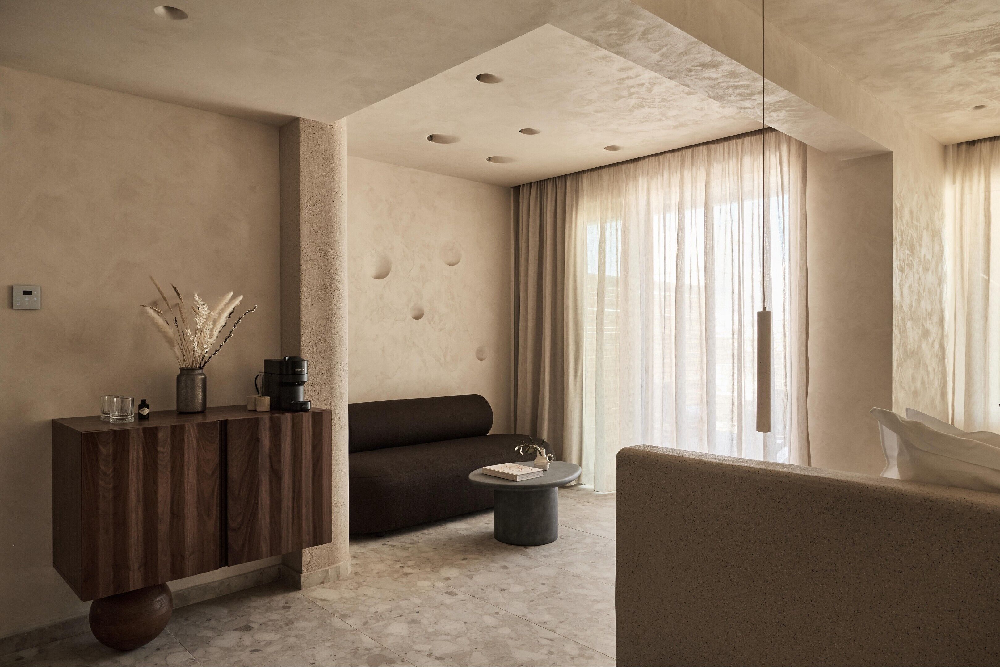 A modern living room with a sofa, a coffee table, a wooden cabinet, and a vase with dried plants.