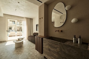 A modern bathroom with a large mirror, a built-in sink, and a view of a pool area. - Uzenie All Suites Boutique Resort - Adults Only (Rethymno)