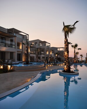 Un hotel moderno con piscina, palmeras y un cielo al atardecer.