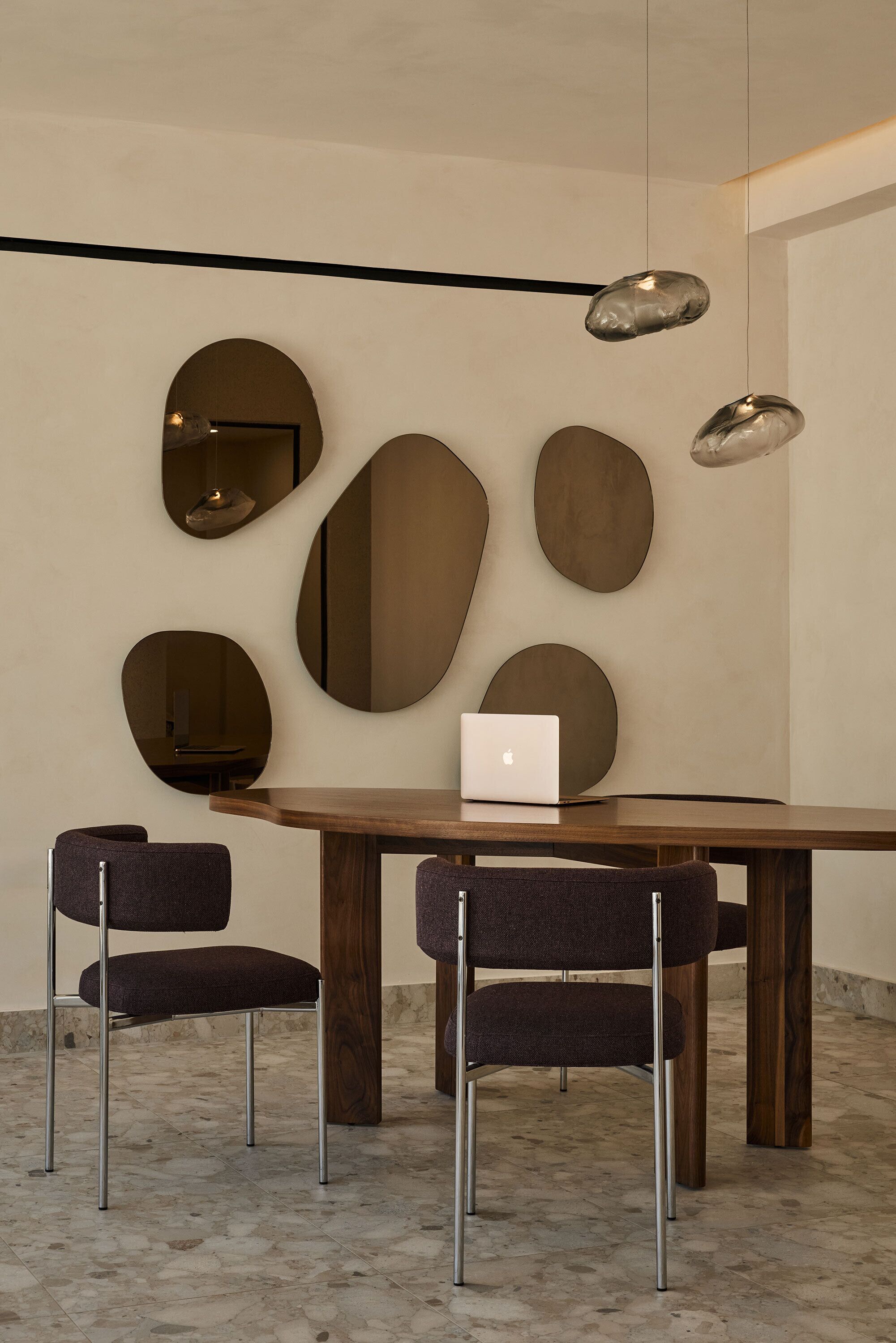 Un comedor moderno con una mesa de madera, dos sillas tapizadas y un ordenador portátil sobre la mesa.