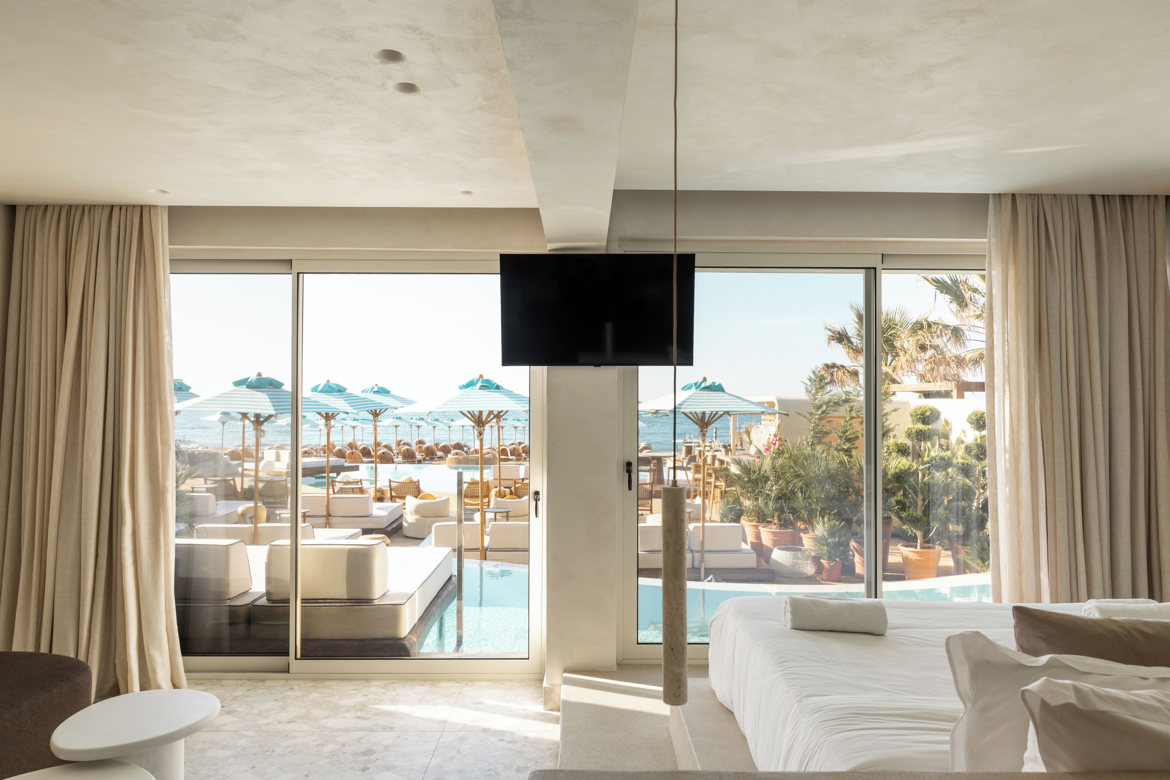 Une chambre d’hôtel dotée d’une grande fenêtre, d’un lit, d’une télévision et offrant une vue sur une piscine et un espace de détente.