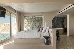 A modern bedroom with a large bed, a stone wall, and a view of the ocean. - Uzenie All Suites Boutique Resort - Adults Only (Rethymno)