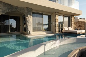 Un área de piscina moderna con agua cristalina, paredes de piedra y un espacio de relax con un sofá blanco.