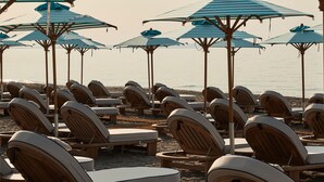 Rows of wooden lounge chairs and striped beach umbrellas on a sandy beach. - Uzenie All Suites Boutique Resort - Adults Only (Rethymno)