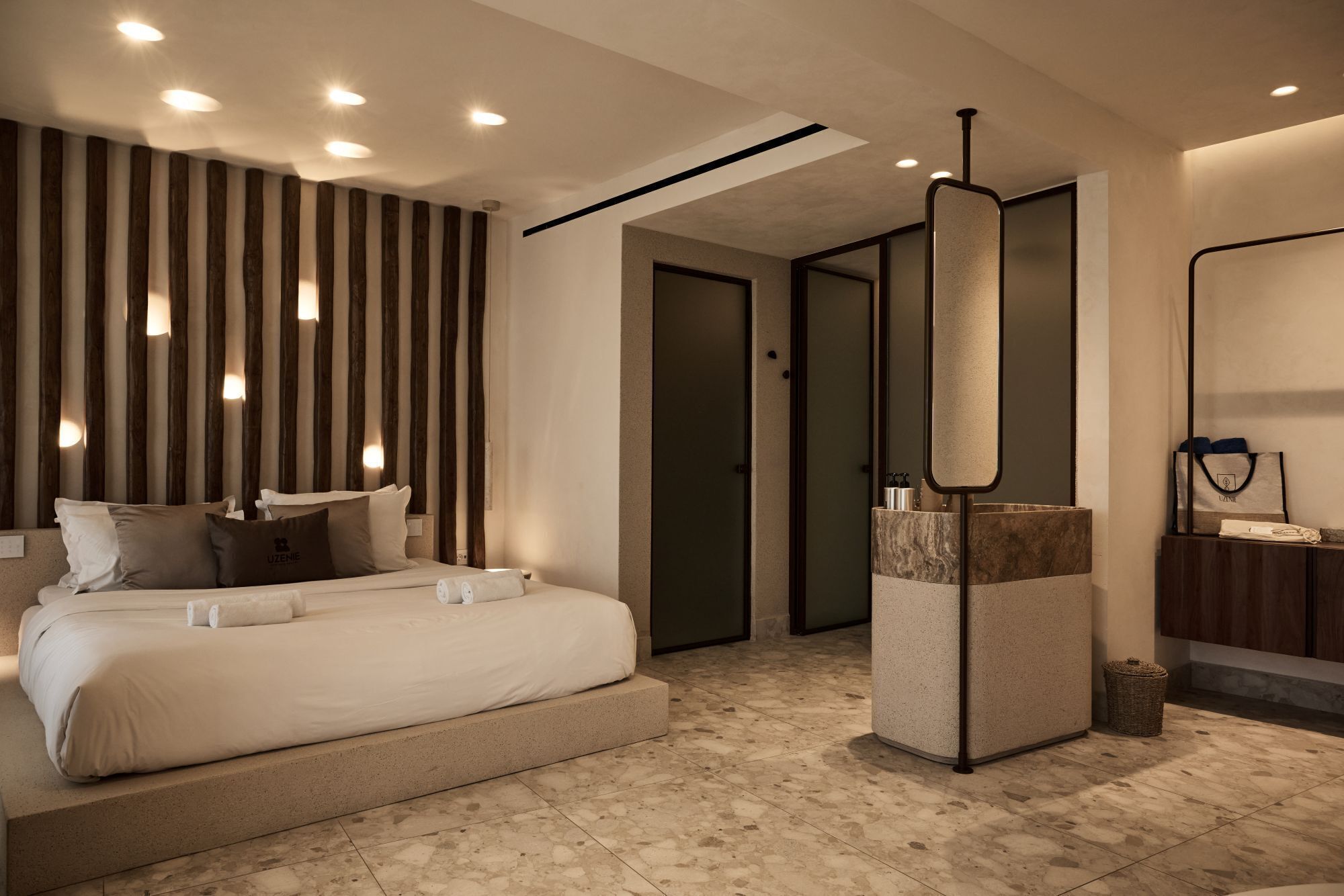 A modern hotel room with a large bed, a built-in wardrobe, a mirror, and a small bathroom area.