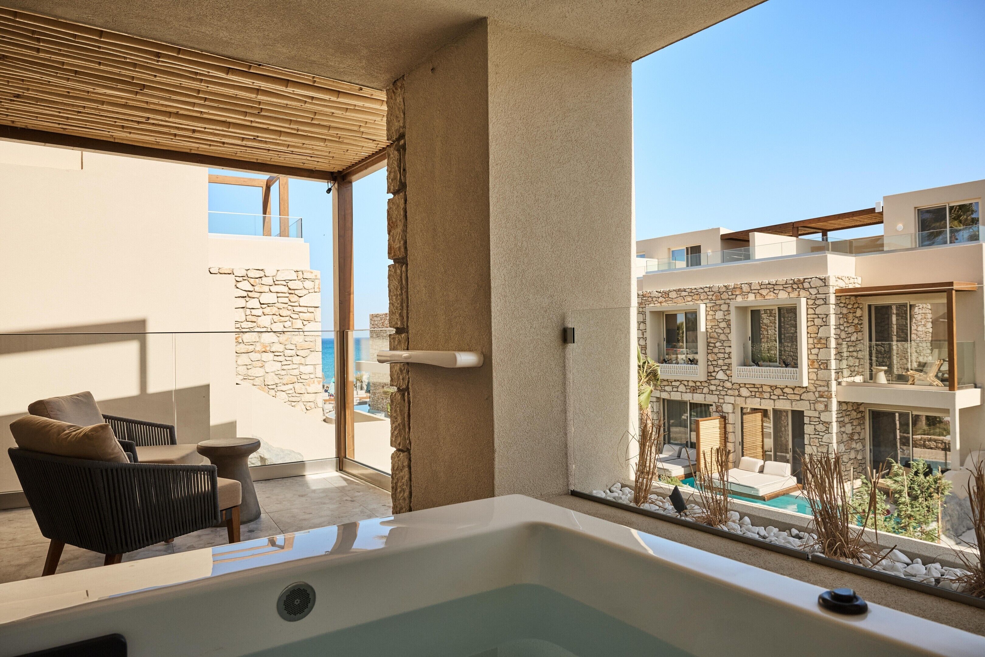 Un área de estar moderna al aire libre con un jacuzzi, paredes de piedra y vistas a una piscina y edificios.