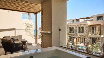Un área de estar moderna al aire libre con un jacuzzi, paredes de piedra y vistas a una piscina y edificios.