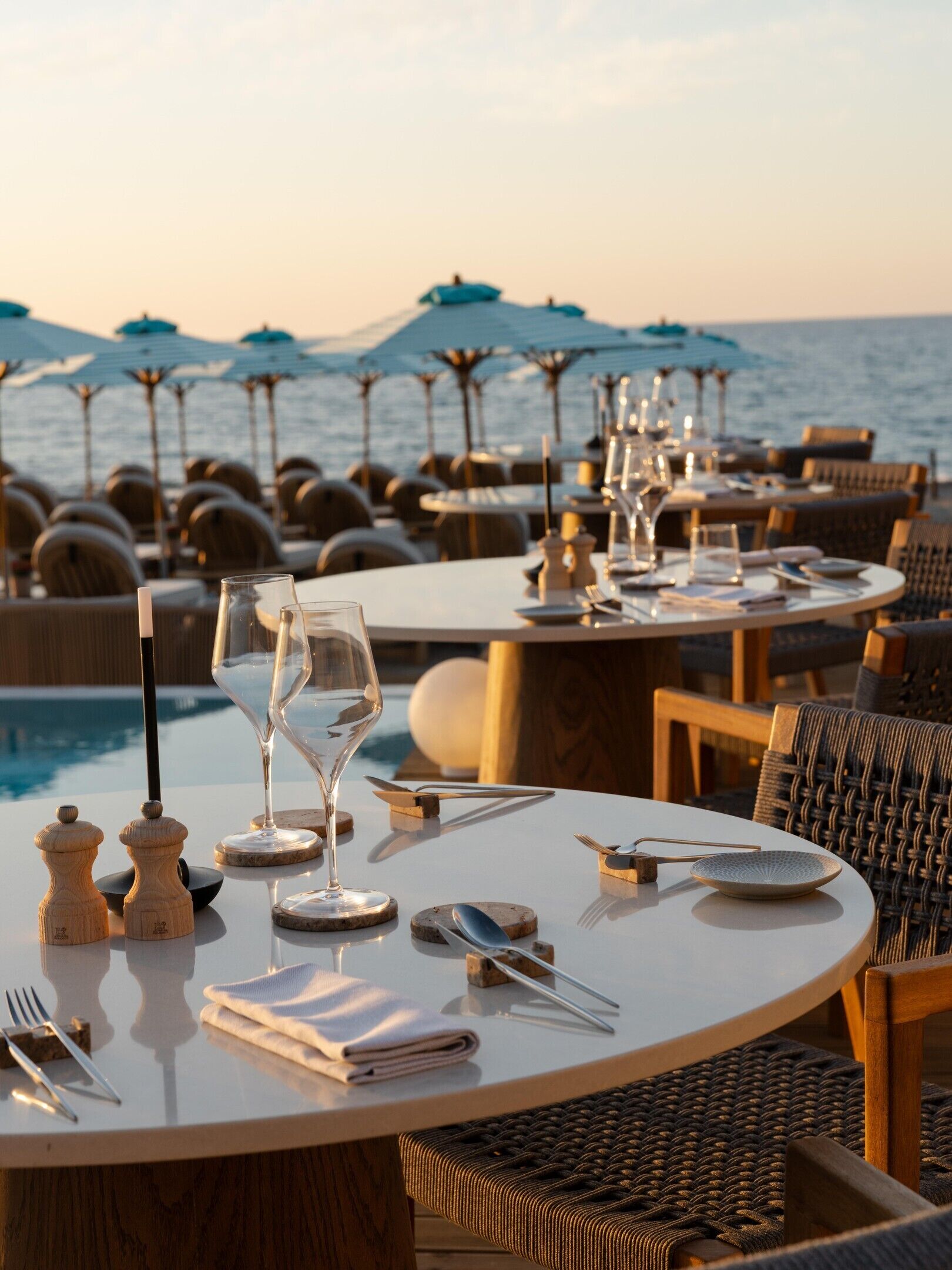 A dining area with tables set for two, overlooking a pool and the sea.