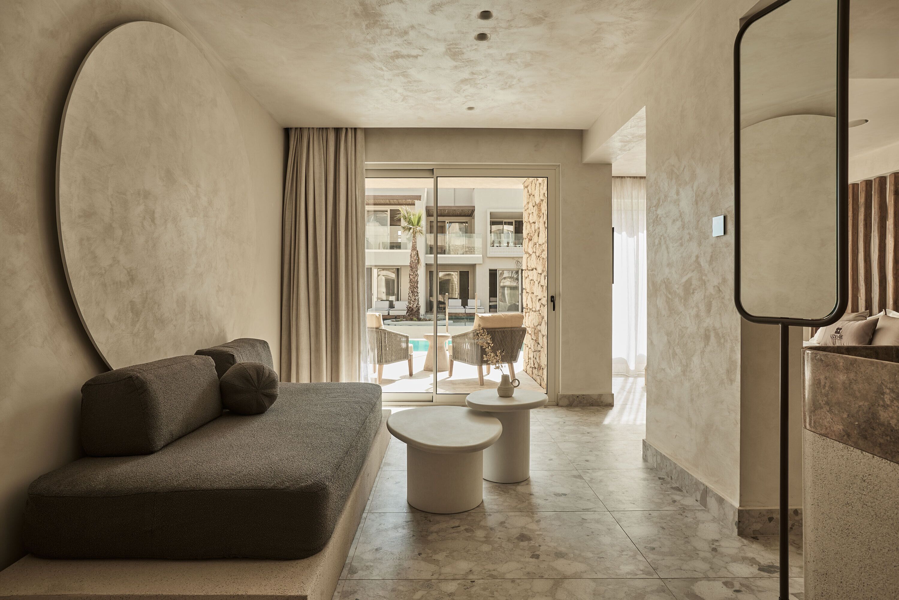 A modern hotel room with a sofa, a small round table, and a large mirror.