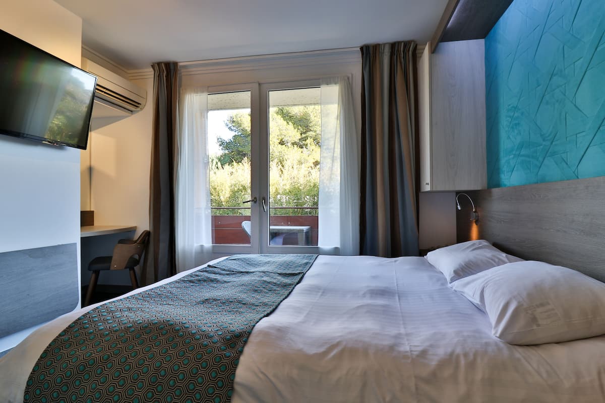 Une chambre d’hôtel avec un lit, un bureau, une télévision et un balcon avec des rideaux.