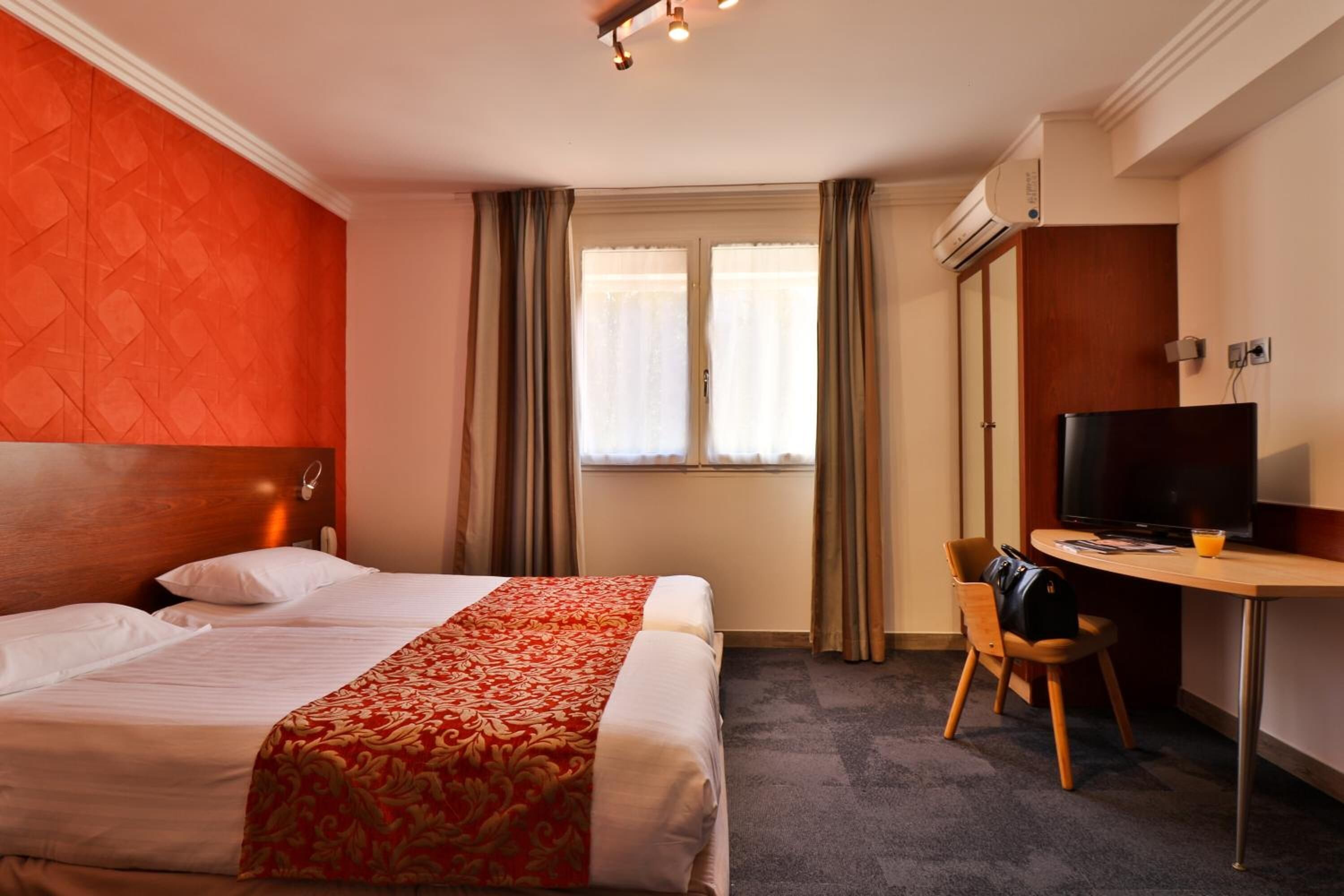 Una camera d'albergo con un letto grande, una scrivania con una sedia, una televisione e una finestra con tende.