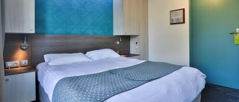 A modern hotel room with a large bed, a built-in skylight, a bedside table with a lamp, and a green door.