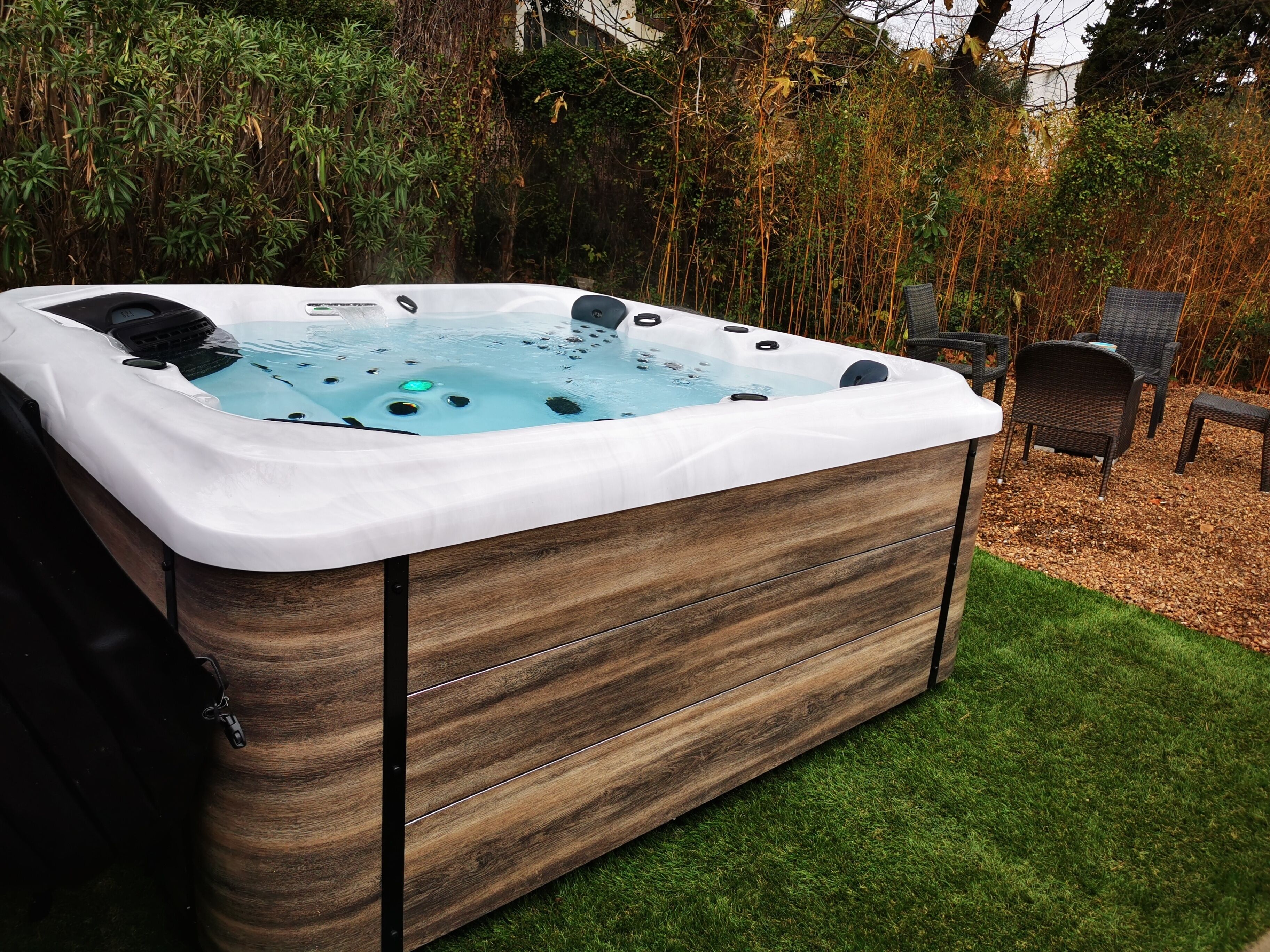 Ein Whirlpool mit Holzverkleidung und Bedienfeld, umgeben von einer Rasenfläche und Stühlen.