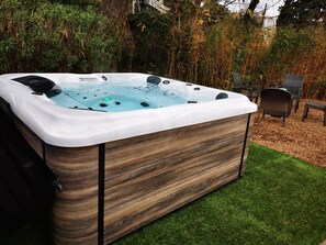 A hot tub with a wooden exterior and a control panel, surrounded by a grassy area and chairs. - Hotel Plage Saint Jean (La Ciotat)