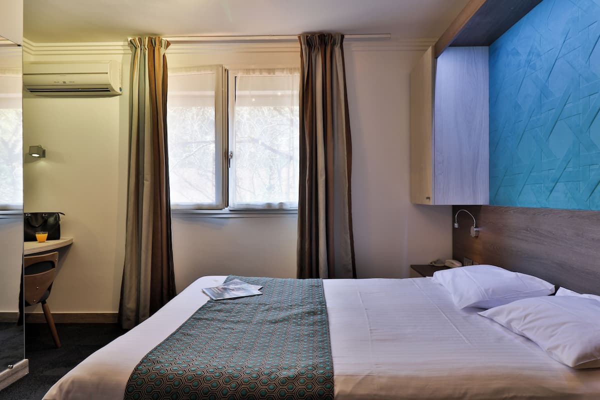 Une chambre d’hôtel avec un lit, un bureau, une chaise et une fenêtre avec des rideaux.