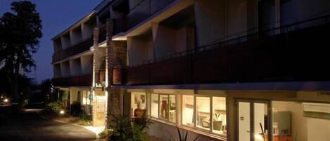 Un hotel de varios pisos con un restaurante en la planta baja y un área de asientos al aire libre visible.