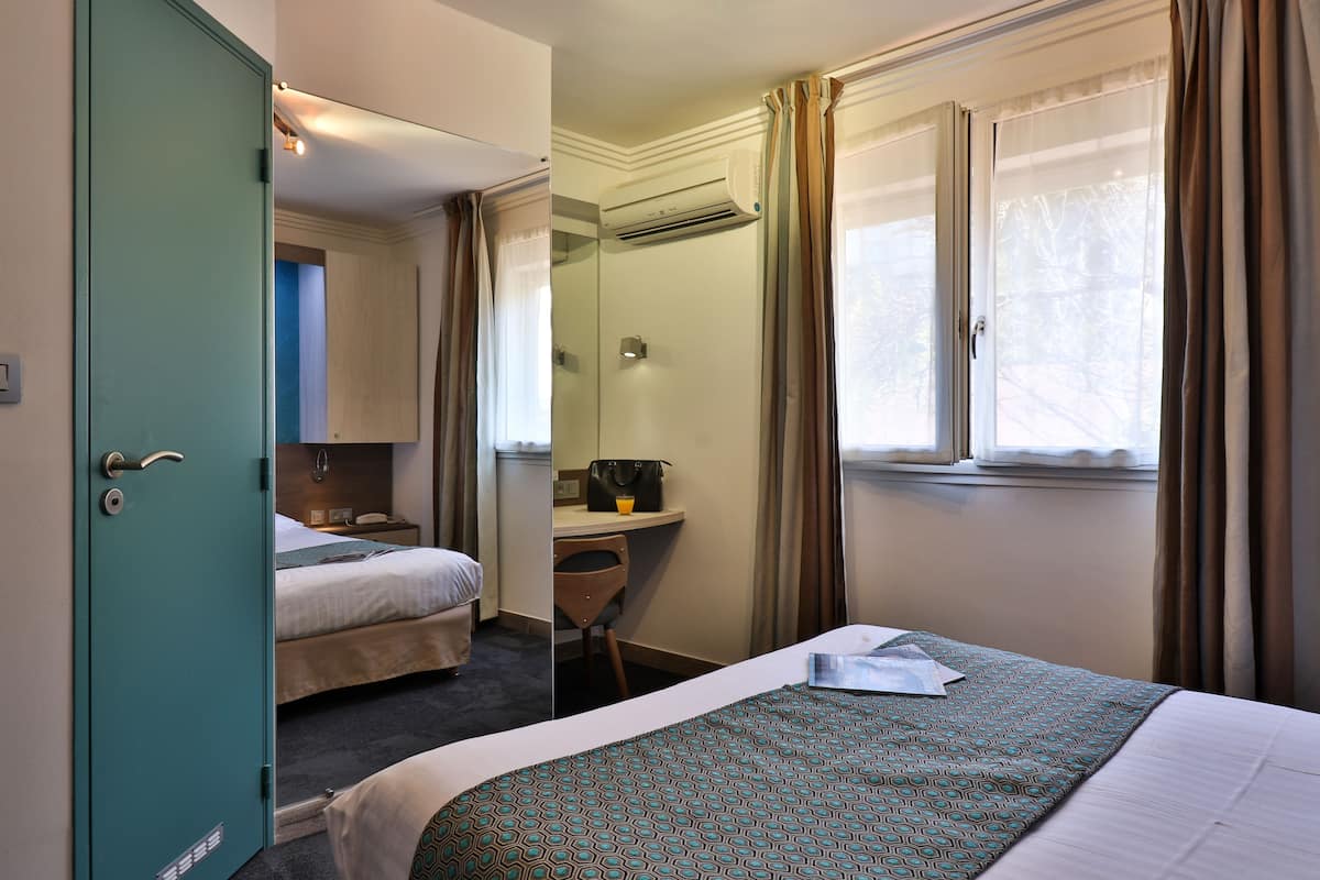 Une chambre d’hôtel avec un lit, un bureau, une chaise et une fenêtre avec des rideaux.