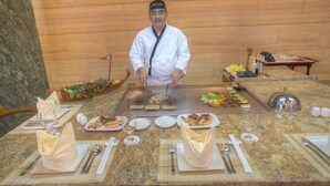 A chef preparing food at a counter with various dishes and utensils. - Siji Hotel Apartment (Al-Fujairah)
