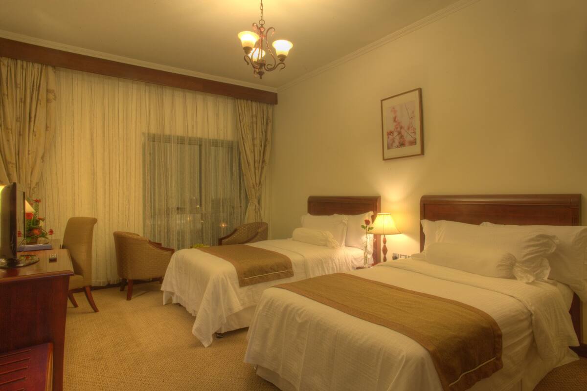 Une chambre d’hôtel avec deux lits, un bureau avec une chaise, une télévision et un lustre.