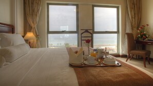 A hotel room with a large bed, a breakfast tray, a chair, and a view of the sea through two windows. - Siji Hotel Apartment (Al-Fujairah)
