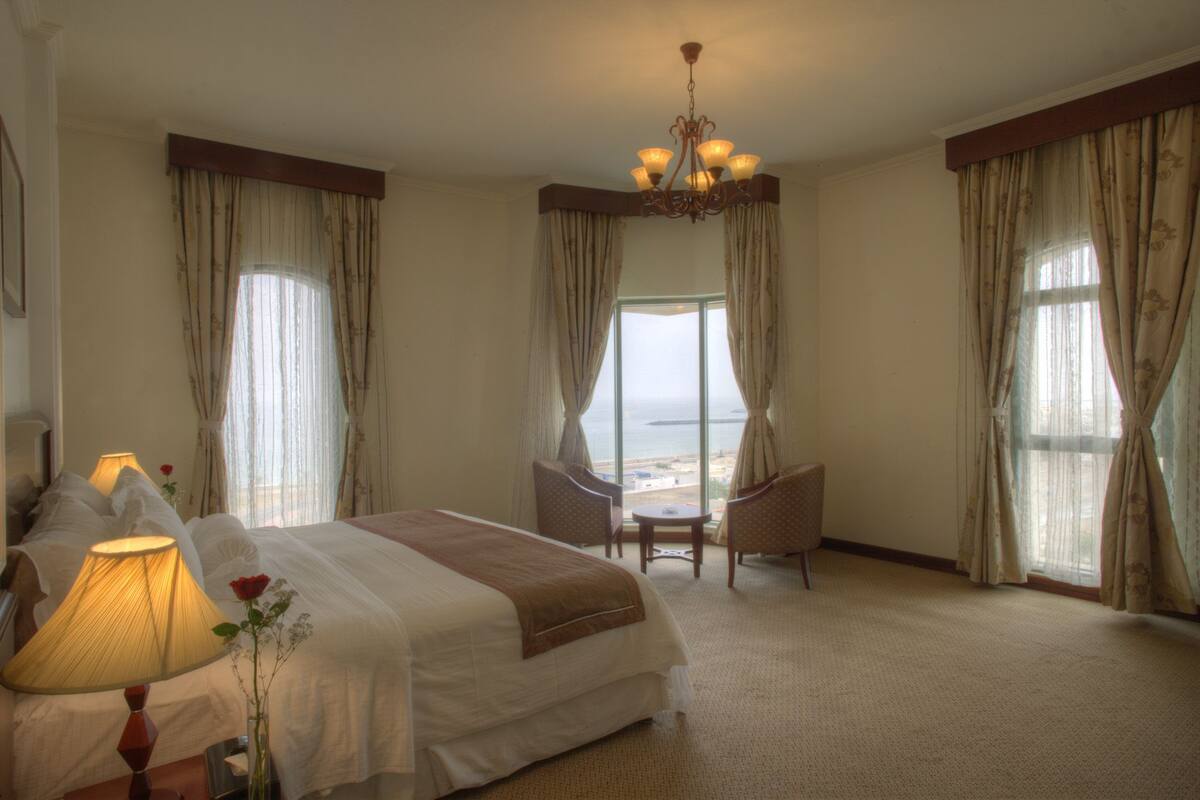 Une chambre d’hôtel avec un lit, un bureau, une chaise, une lampe et une vue sur la mer.