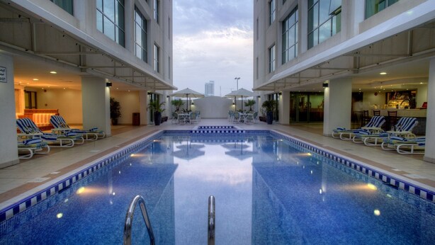 A large indoor swimming pool with lounge chairs and umbrellas, surrounded by a modern building with large windows. - Siji Hotel Apartment (Al-Fujairah)