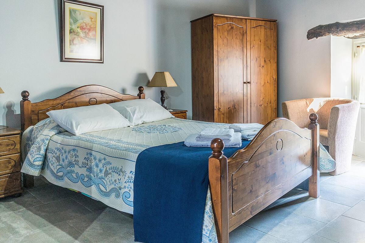 Ein Schlafzimmer mit einem hölzernen Bett, einem Nachttisch, einer Lampe, einem Kleiderschrank und einem Sessel.