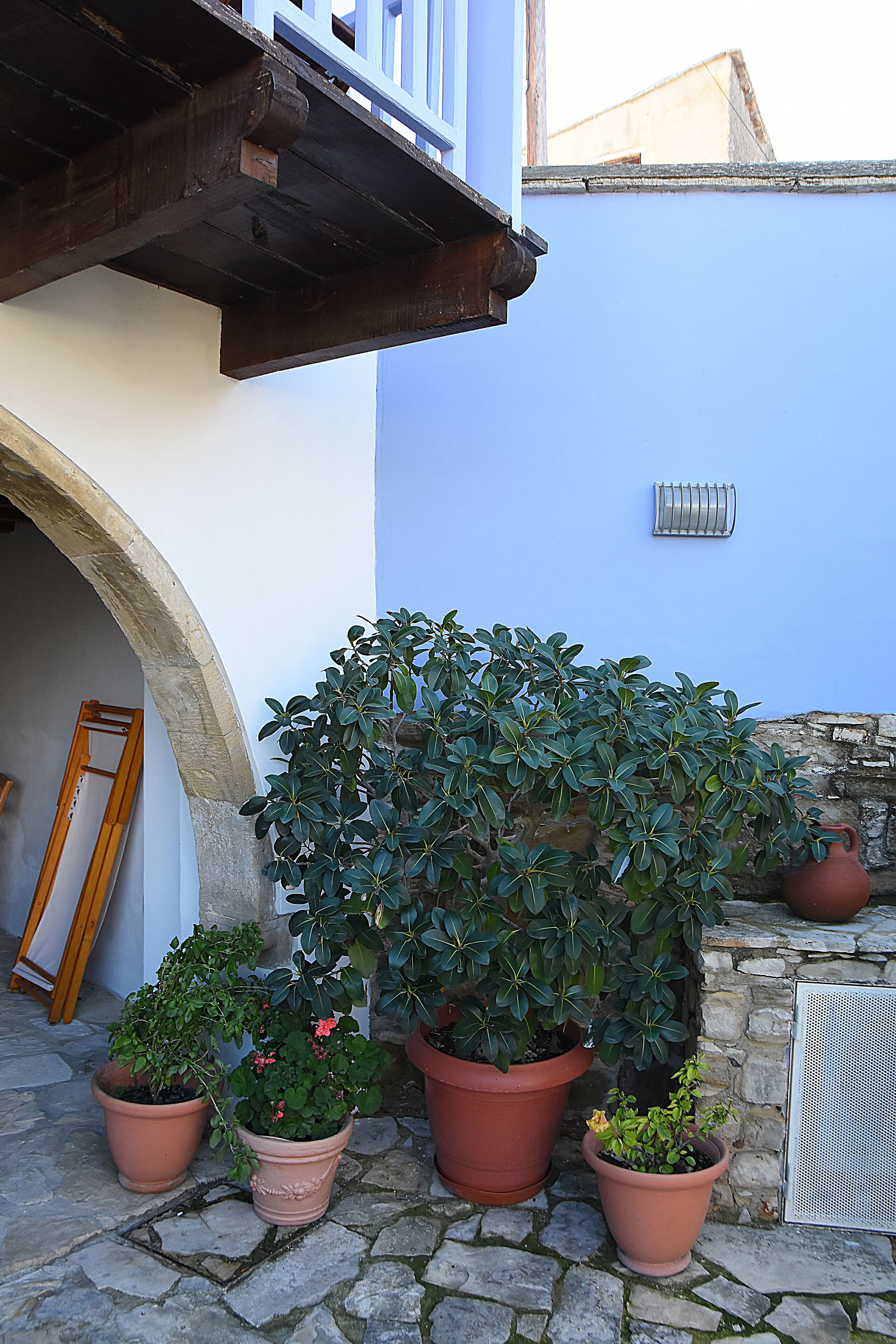 A courtyard with potted plants, a stone wall, and a blue building facade.