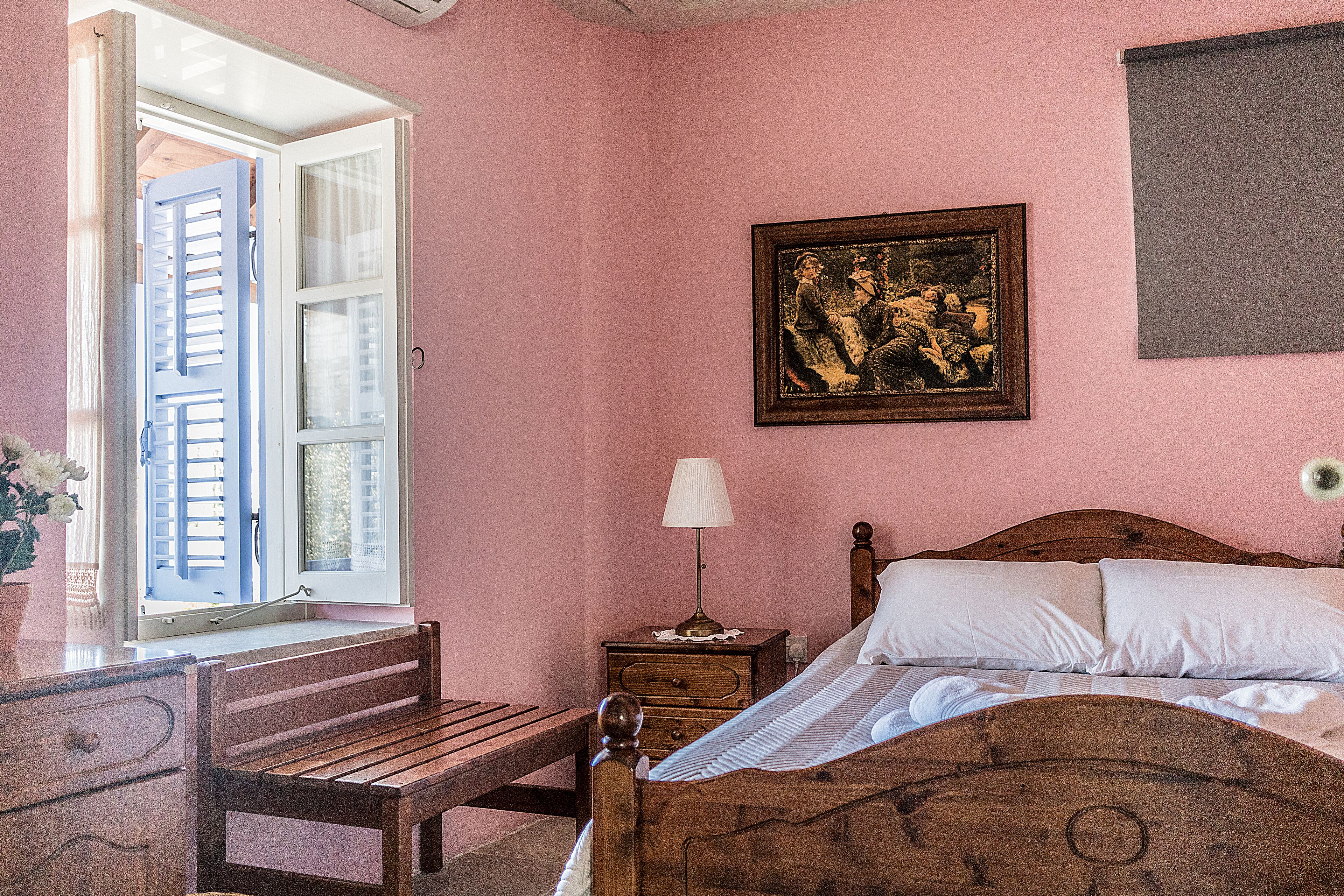 Une chambre à coucher avec un lit en bois, une table de chevet avec une lampe, un banc et une fenêtre avec des volets.
